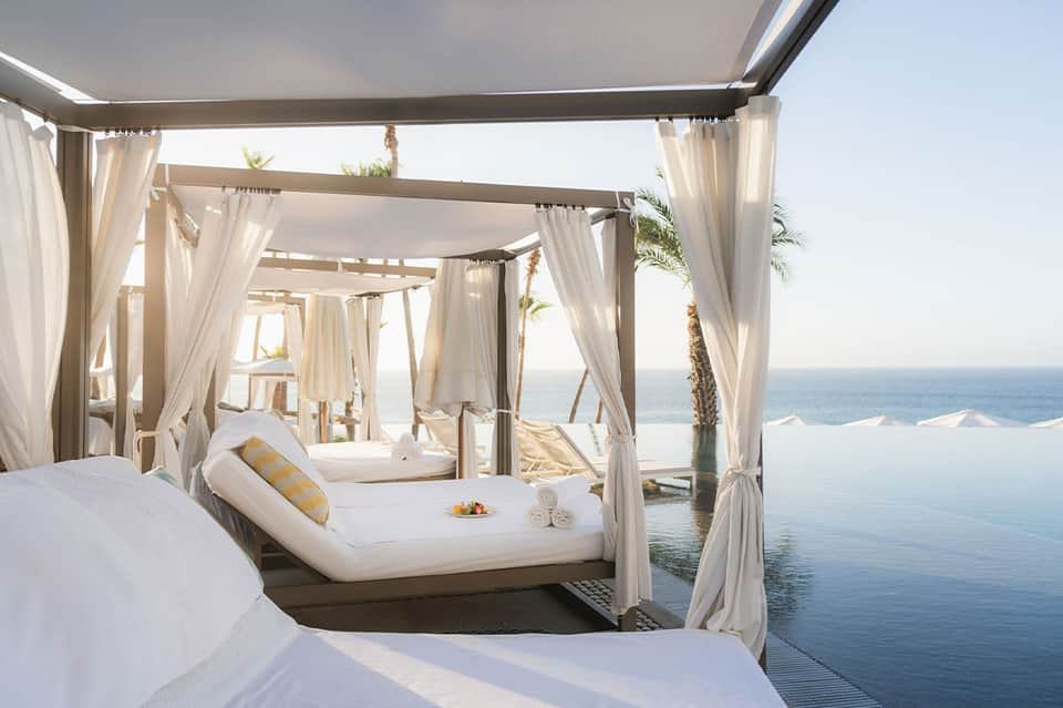 Luxury beachfront cabana beds with flowing white curtains overlooking infinity pool and ocean