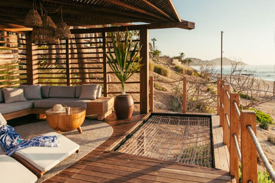 Elevated wooden deck with gray cushioned seating, pergola shade, and coastal ocean views