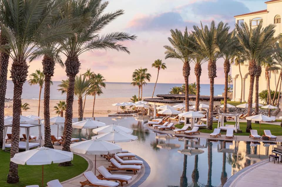 Luxurious beachfront resort pool with loungers, umbrellas, and palm trees