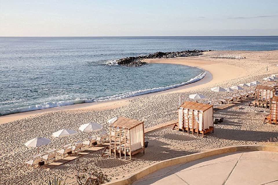 Sandy beach with wooden beach cabanas, umbrellas, calm ocean waters, and coastal landscape