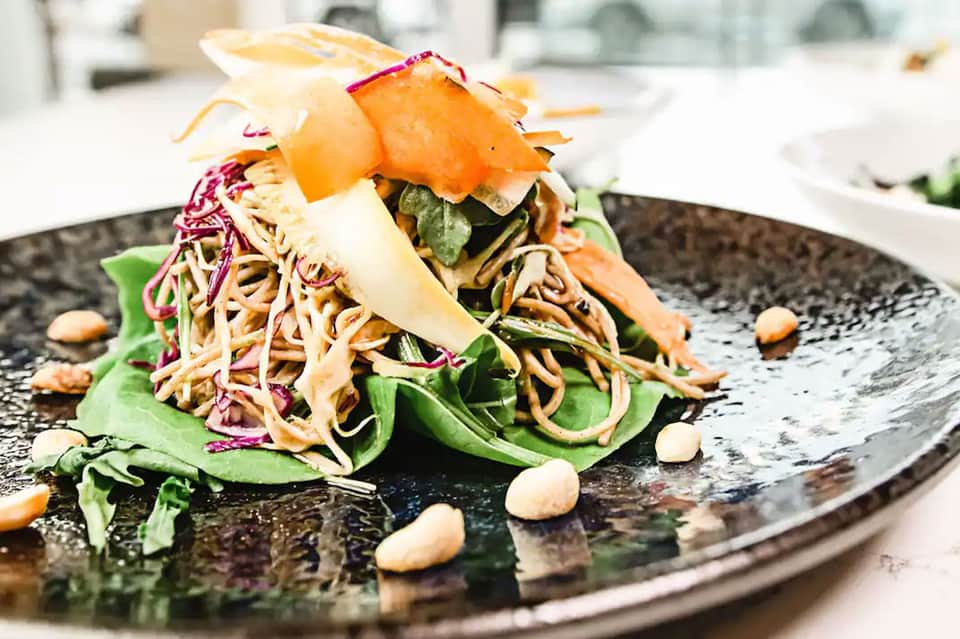 Gourmet plated salad dish with seared protein, crispy noodles, and fresh greens on dark plate