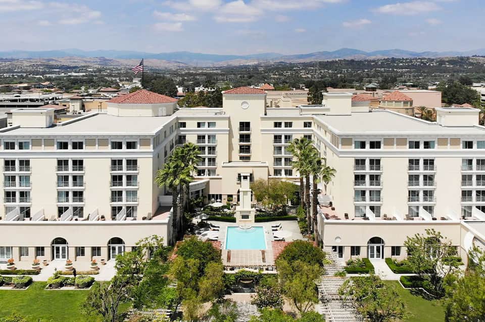Aerial view of white resort complex with central courtyard pool surrounded by palm trees