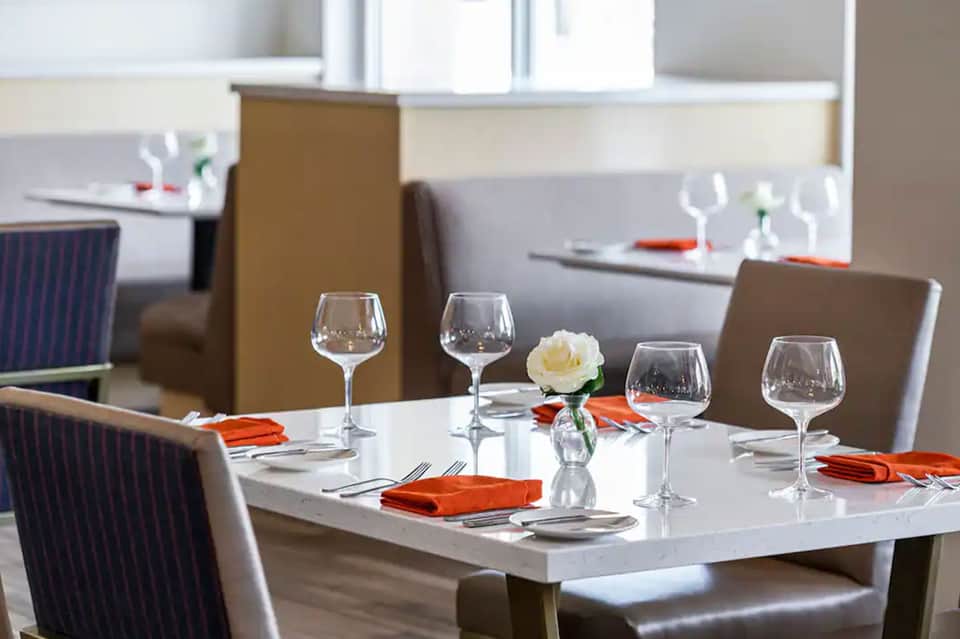 Elegant dining table set with wine glasses, white flower centerpiece, and orange napkins