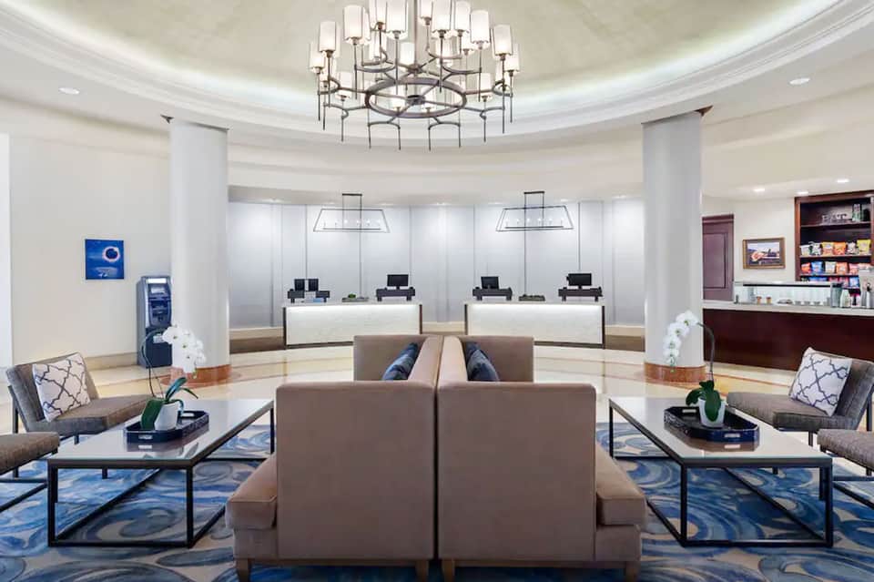 Elegant hotel lobby with circular chandelier, reception desks, comfortable seating, and polished floors