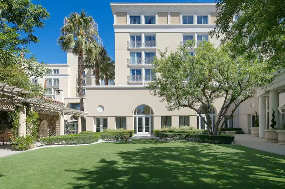 Modern resort building with manicured lawn, palm trees, and classical architecture