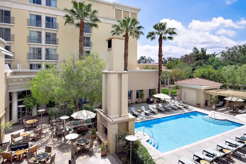 Resort courtyard pool with lounge chairs, umbrellas, palm trees, and hotel building