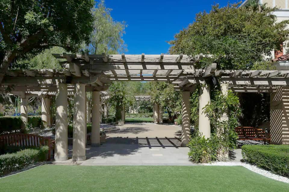Garden pergola pathway with white lattice structure, green landscaping, and sunny blue sky
