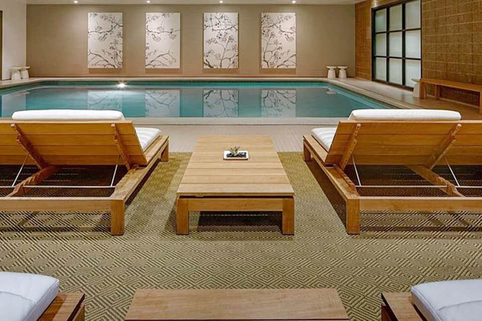 Indoor pool with wooden loungers, lounge chairs, and calming water feature in spa area