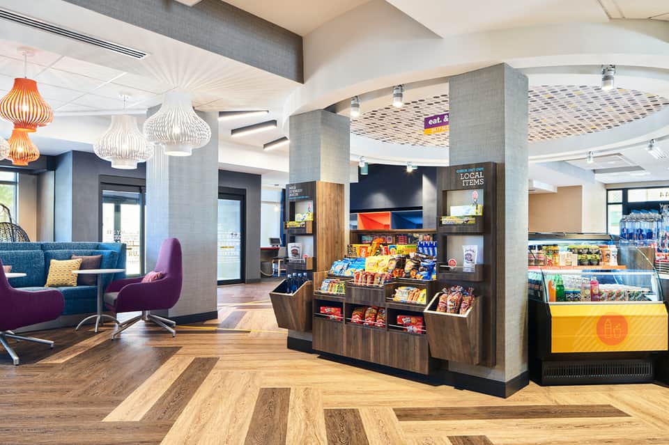 Modern hotel lobby with blue seating, pendant lights, retail displays, and contemporary furnishings