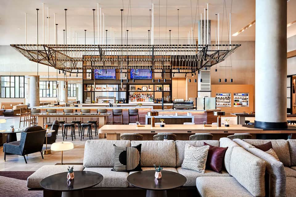 Modern hotel lobby and bar with high ceilings, geometric net-like design element, seating areas, and wooden accents