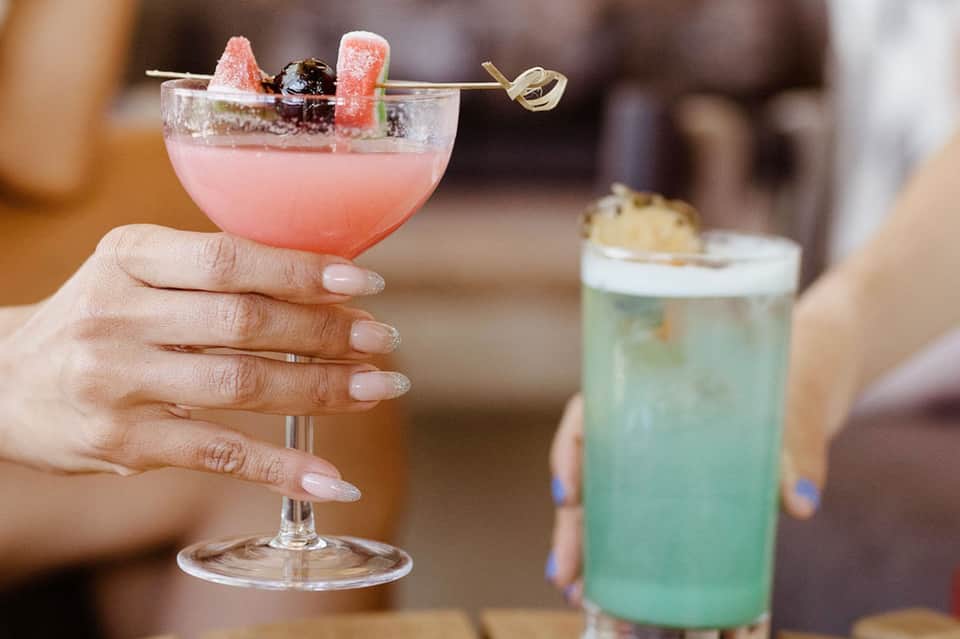 Colorful cocktails with pink drink and mint garnish held in hand