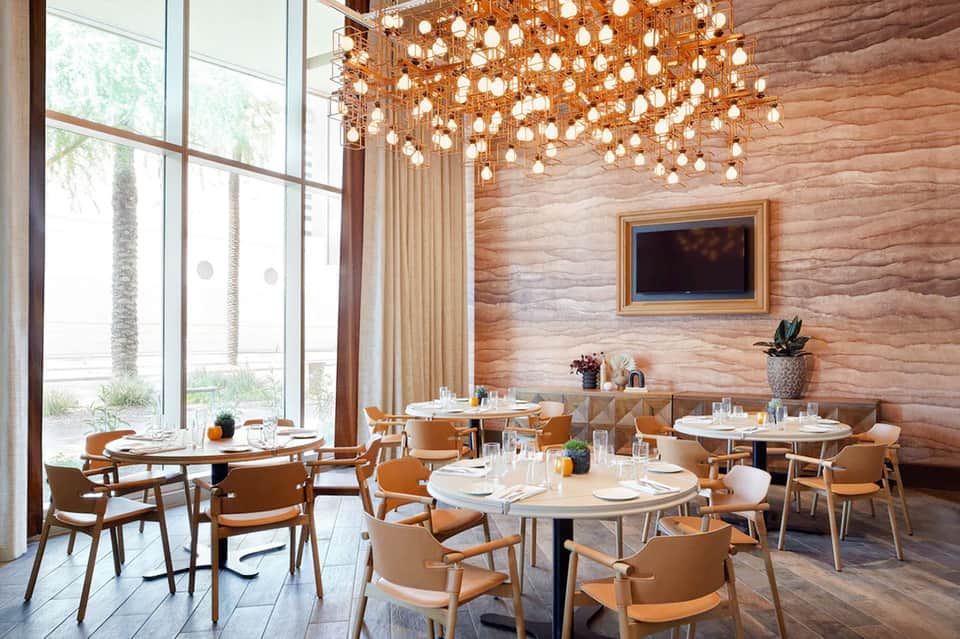 Upscale restaurant interior with wooden walls, amber pendant lights, round tables, and large windows