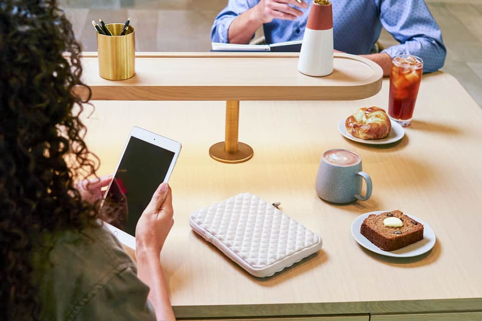 Casual café setting with wooden table, coffee cup, pastries, and person using tablet device