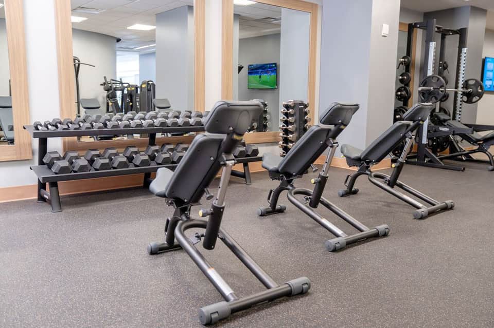 Hotel fitness center with weight racks, dumbbells, exercise bikes, and wall-mounted TV