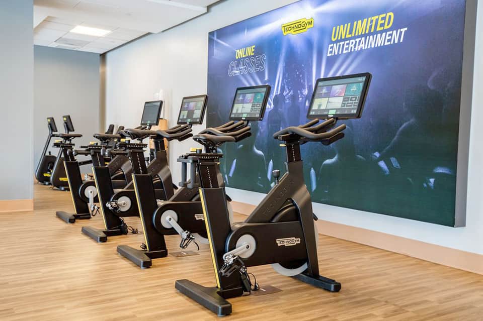 Fitness center with stationary bikes and digital screens displaying entertainment