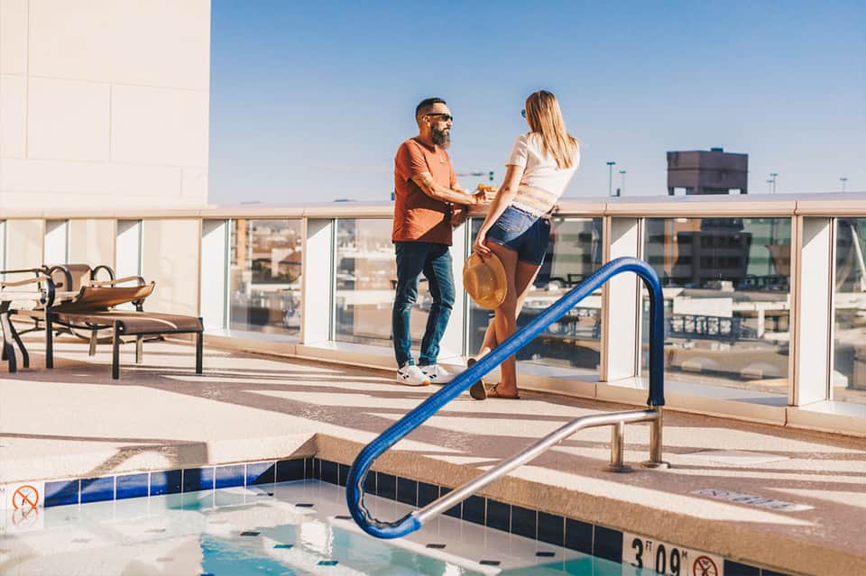 Two people on rooftop deck overlooking city with indoor pool in foreground