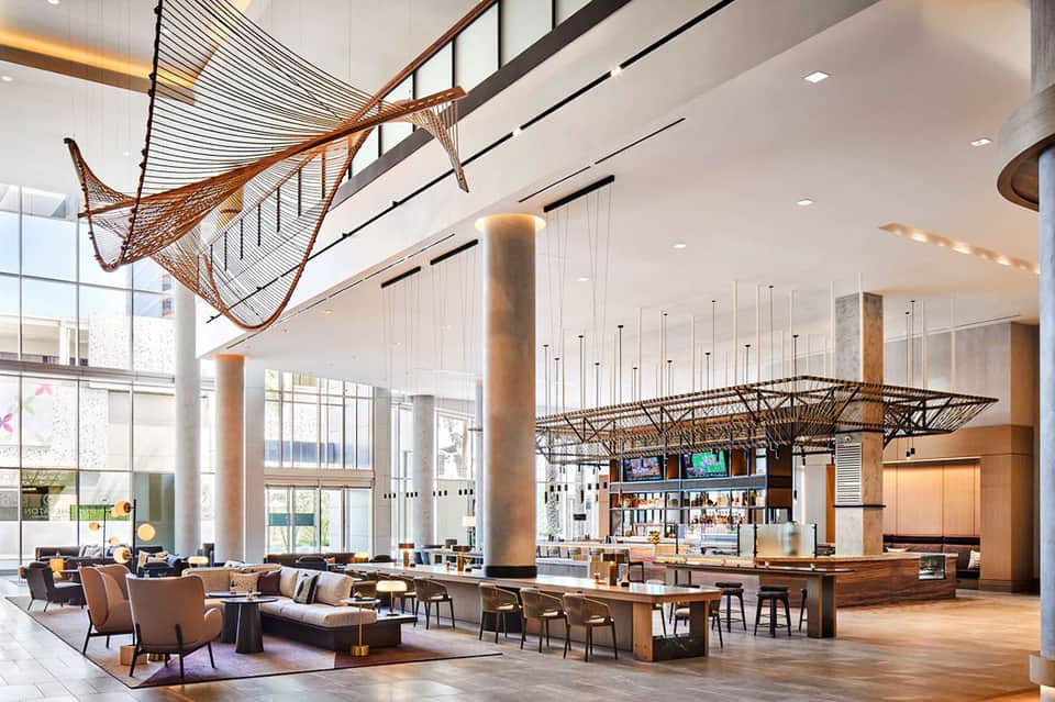 Modern hotel lobby with high ceilings, decorative fishing nets, and contemporary bar area