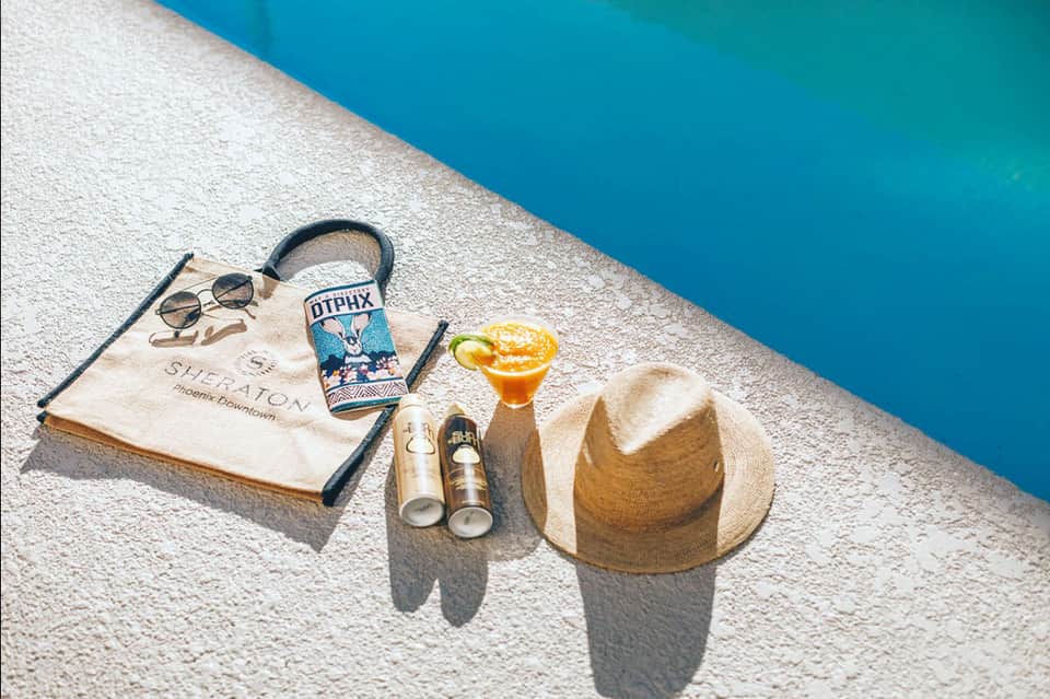 Poolside flat lay with sunglasses, hat, towel, and tropical cocktail