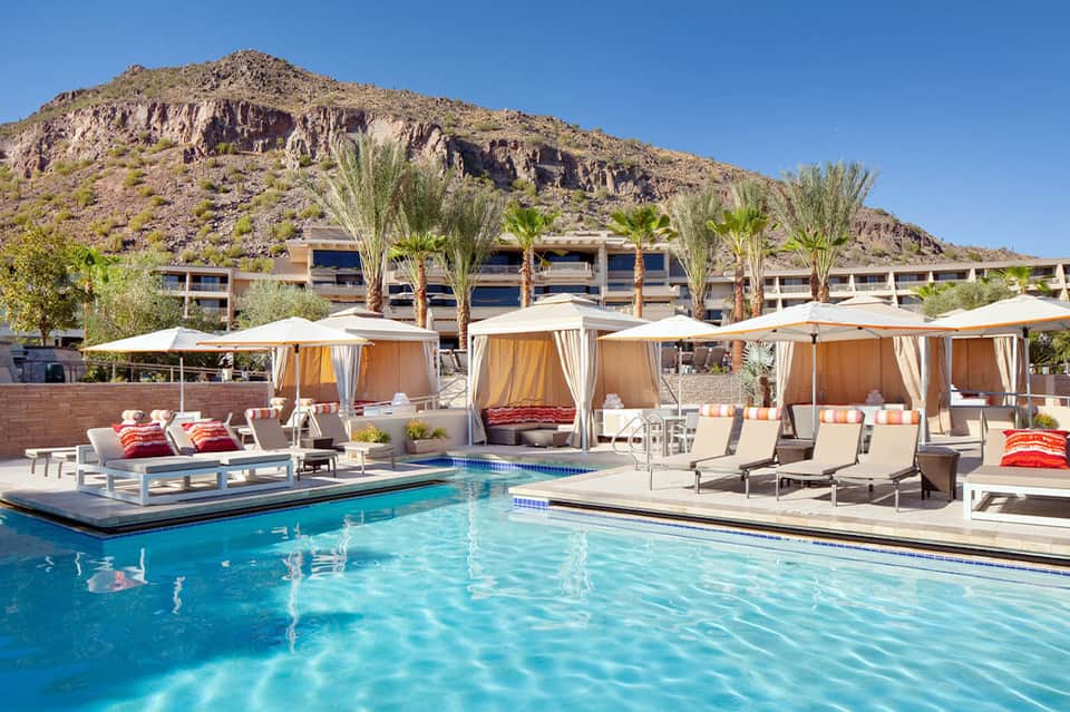 Desert resort pool with turquoise water, cabanas, lounge chairs, and mountainside backdrop