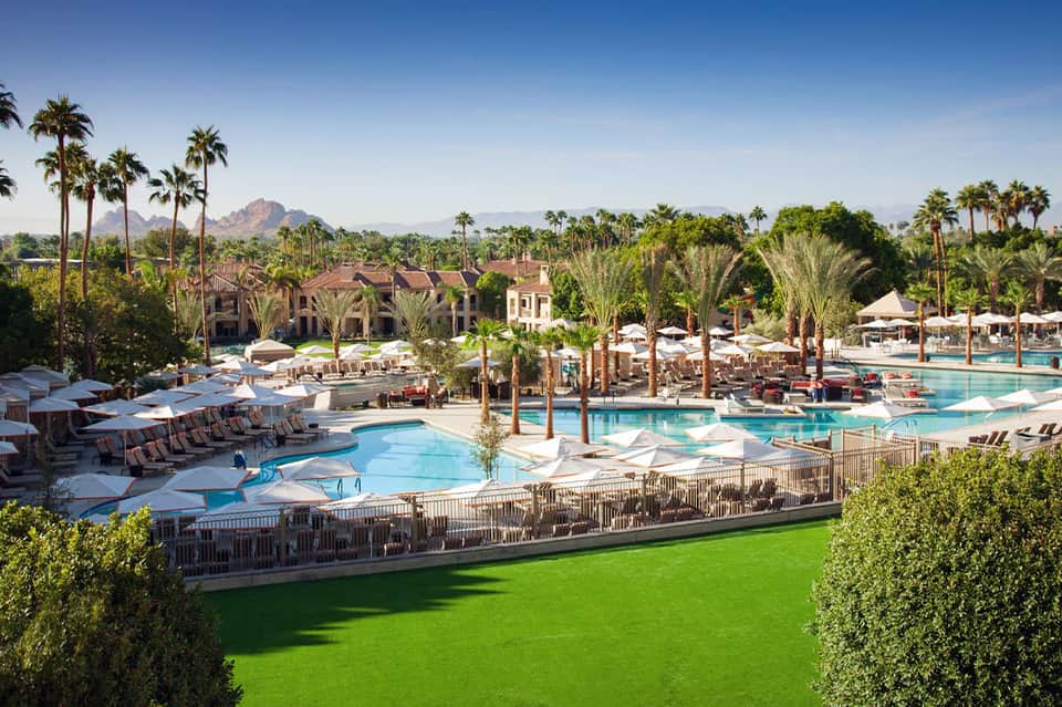Expansive resort with multiple pools, palm trees, loungers, and desert mountains in distance