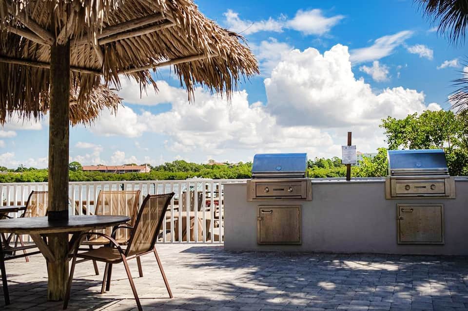 Outdoor deck with grilling station, tiki umbrella, lounge chairs, and waterfront view