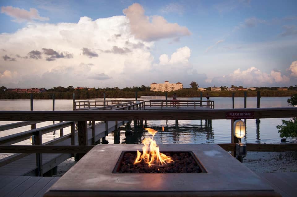 Waterfront fire pit with dock overlooking calm bay and resort building at dusk