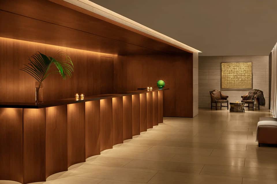 Elegant hotel lobby with warm wood paneling, reception desk with ambient lighting, and sitting area with leather chairs