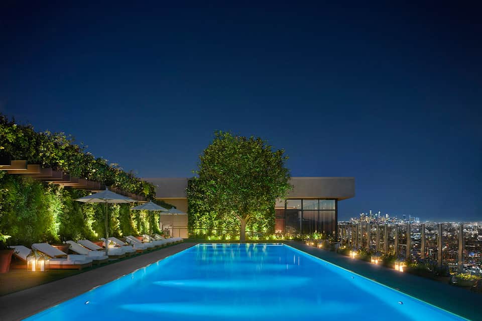 Illuminated rooftop infinity pool at night with city lights and lounge seating area