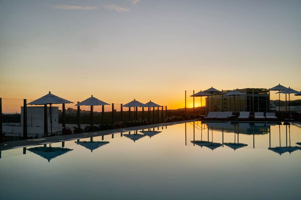Infinity pool at sunset reflecting umbrellas and cabanas under golden sky