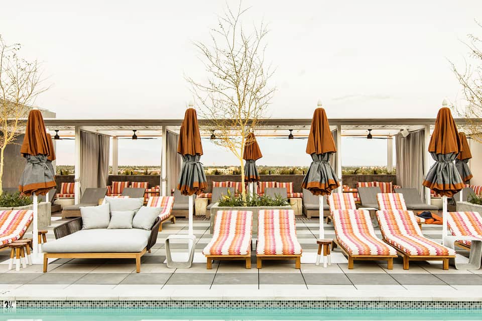 Poolside lounge area with striped chaise lounges, umbrellas, pergolas, and modern seating furniture