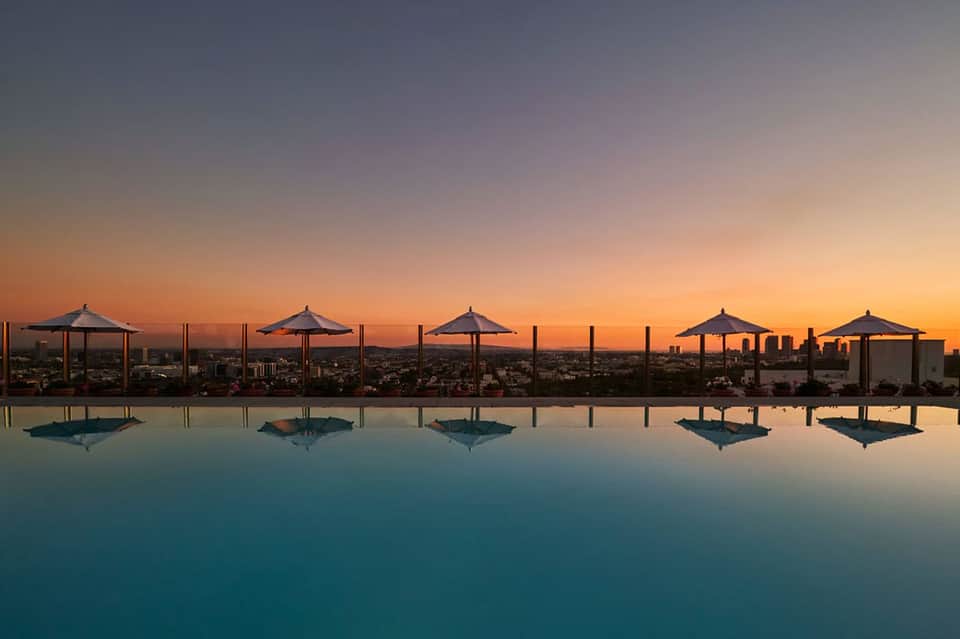 Infinity pool at dusk with umbrellas and city skyline reflection at sunset