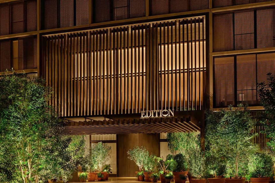 Modern hotel entrance 'EDITION' with vertical wood slat design and lush climbing ivy landscaping