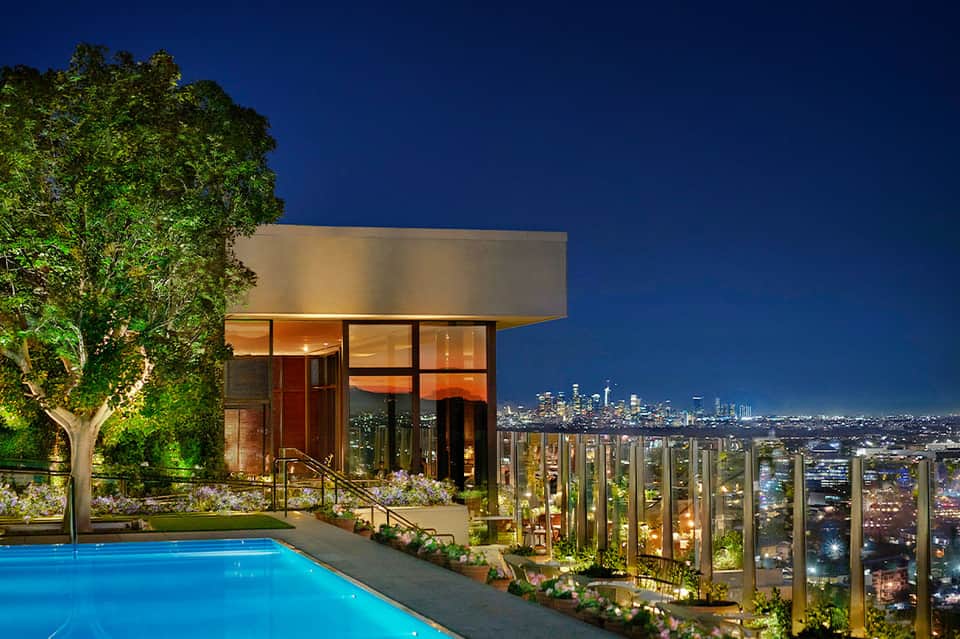 Hillside residence with illuminated infinity pool, modern architecture, and panoramic city skyline at night