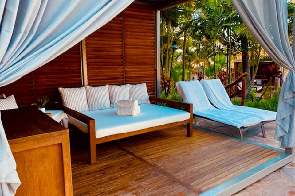 Covered wooden deck with cushioned seating, blue and white striped furnishings, and tropical plants