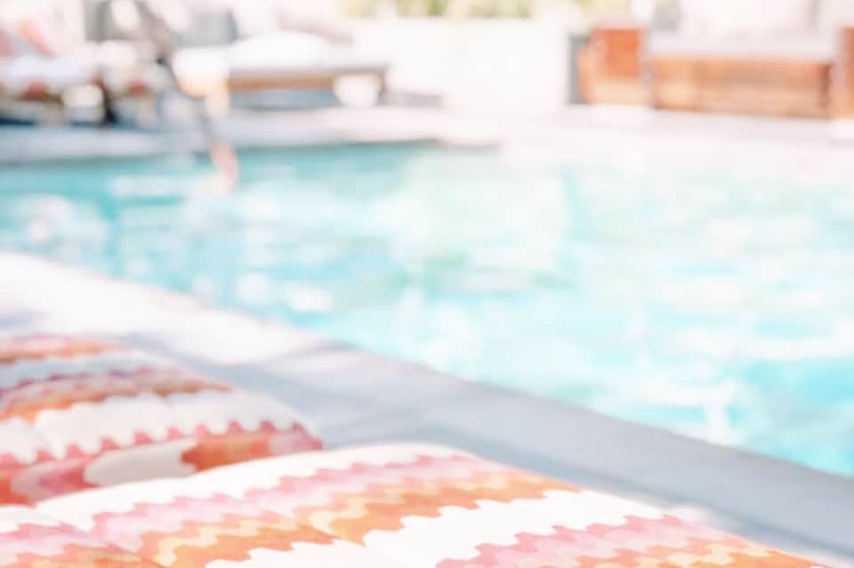 Colorful patterned towels on lounge chair beside bright turquoise swimming pool