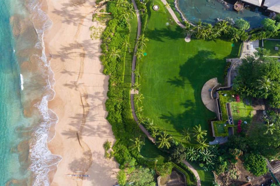 Aerial beach view showing sandy shore, turquoise water, manicured resort grounds with palm trees