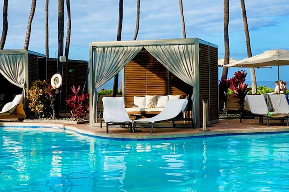 Luxury pool cabana with white curtains, lounge chairs, and ocean backdrop