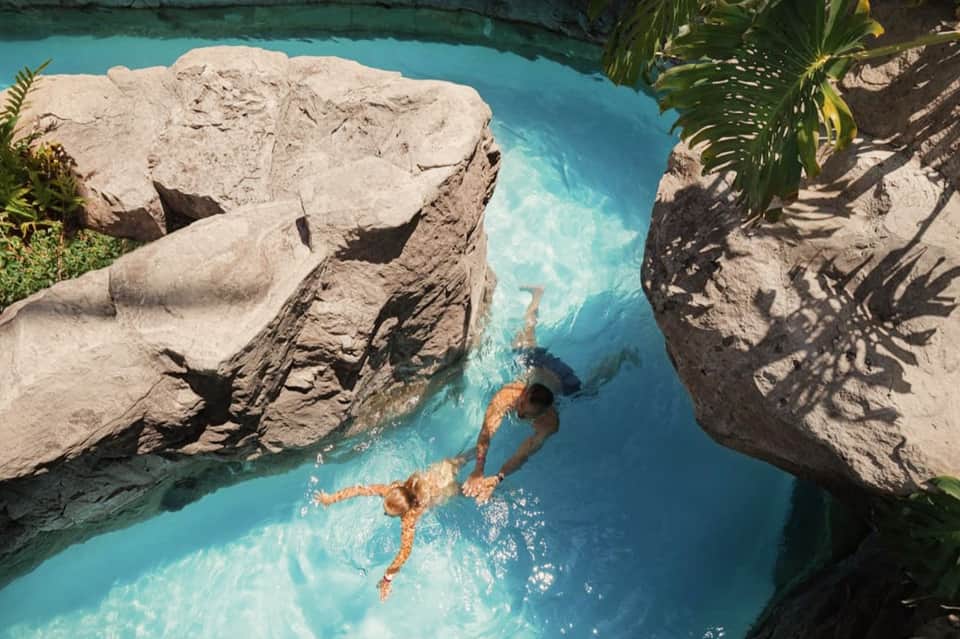 Person swimming in turquoise natural pool surrounded by white limestone rocks and tropical vegetation
