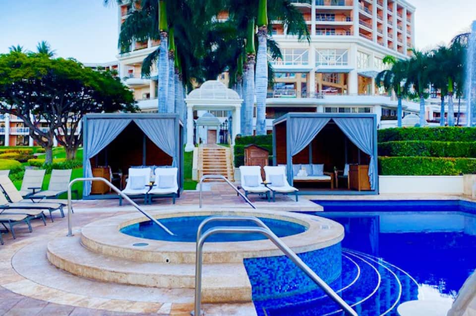 Luxury pool area with white cabanas, spa tub, and high-rise resort building backdrop