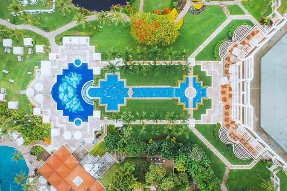Aerial view of resort pool complex featuring blue cross-shaped pools surrounded by manicured lawns