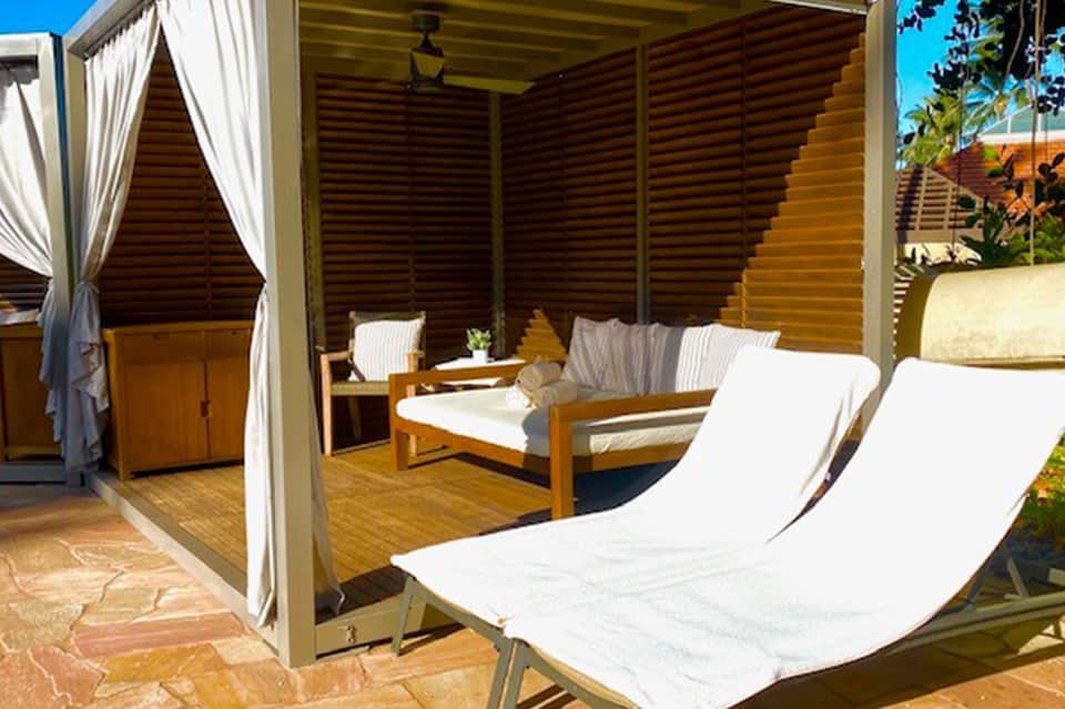 Luxury cabana with lounge chairs, sheer curtains, wooden furnishings, and private outdoor space