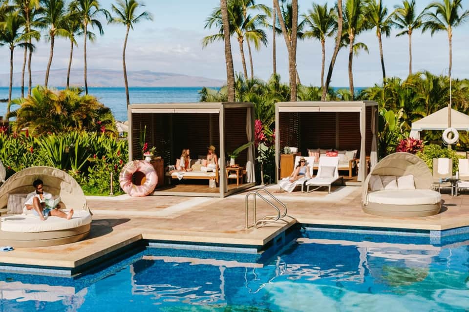 Oceanfront resort pool with cabanas, loungers, and tropical palm landscape