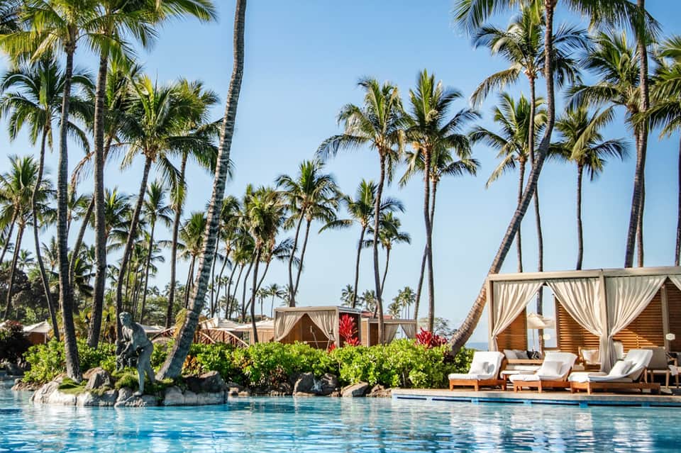Resort pool with cabanas, palm trees, and lounge chairs overlooking tropical ocean landscape