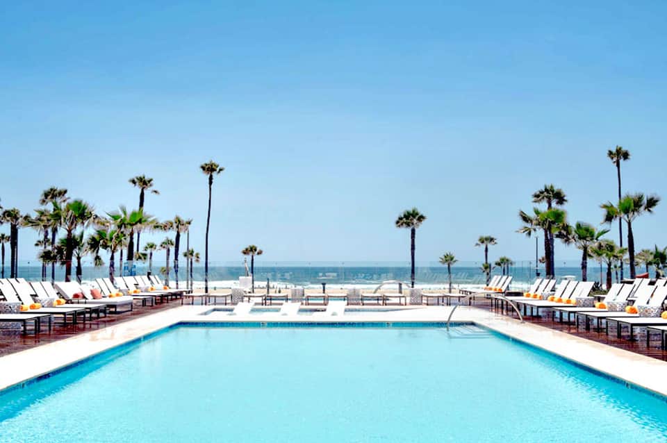 Resort pool with palm trees and ocean view, white lounge chairs lining the deck