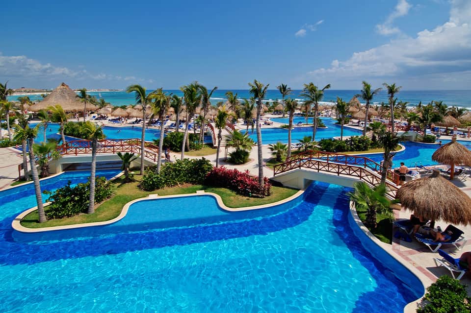 Expansive all-inclusive resort pool complex with palm trees and ocean view