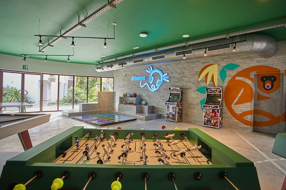 Recreation room with green foosball table, arcade games, ping pong table, and neon signage