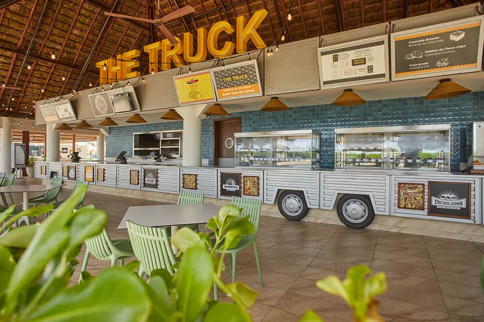 Colorful food truck venue with green chairs, yellow signage, and modern covered dining area
