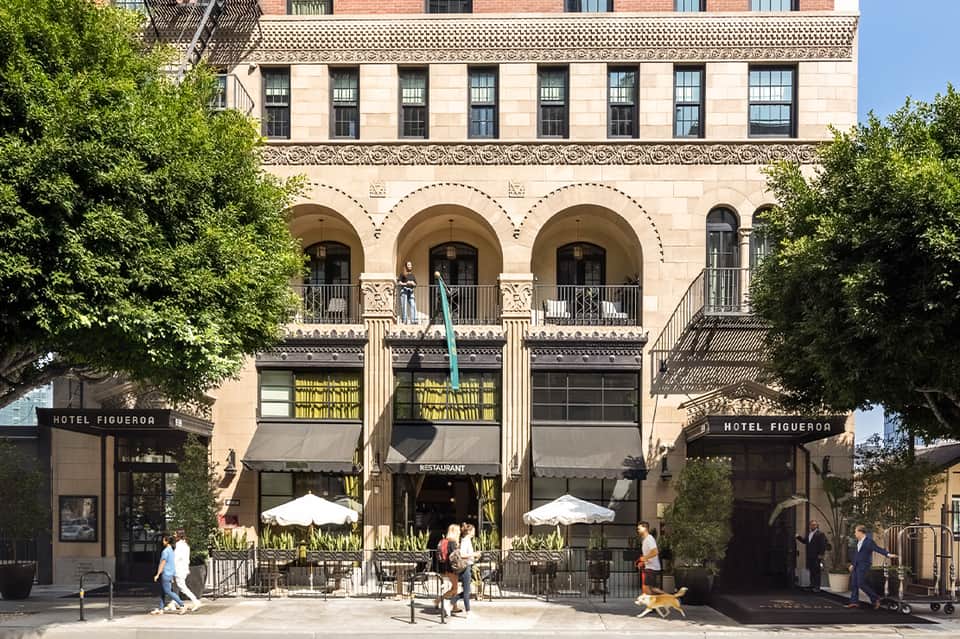 Historic hotel building facade with arches, columns, green awnings, and outdoor dining area