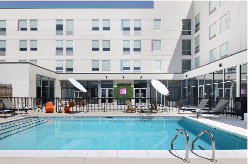 Modern hotel indoor pool surrounded by white buildings, large windows, and contemporary seating