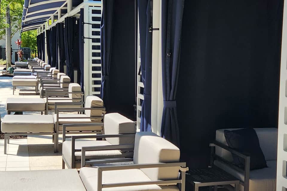 Row of lounge chairs with white cushions along resort deck under black shade structures